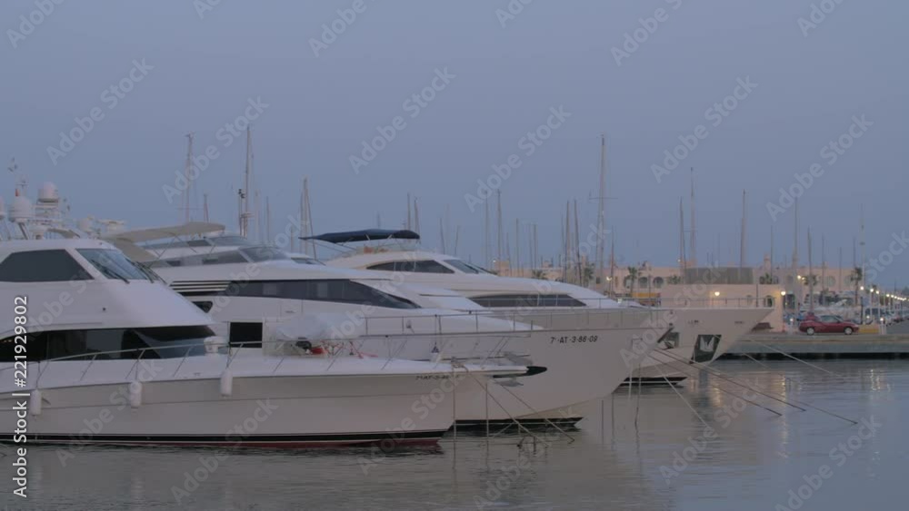 ALICANTE, SPAIN - APRIL 19, 2018: Panning shot of port in the city. View to many moored yachts and motor boats., evening scene ALICANTE, SPAIN - APRIL 19, 2018: Panning shot of port in the city. View to many moored yachts and motor boats., evening scene
