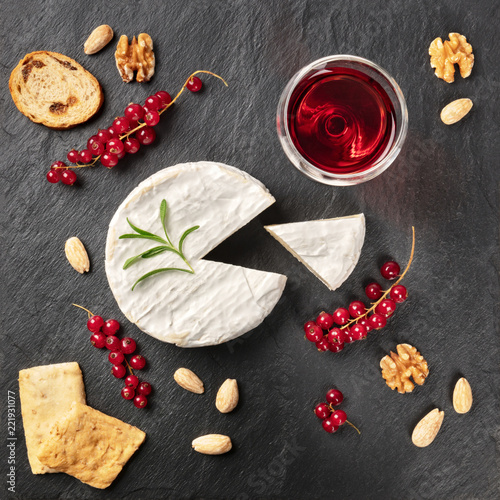 An overhead photo of Camembert cheese with a glass of red wine, fruits and nuts, shot from above on a black background with copy space