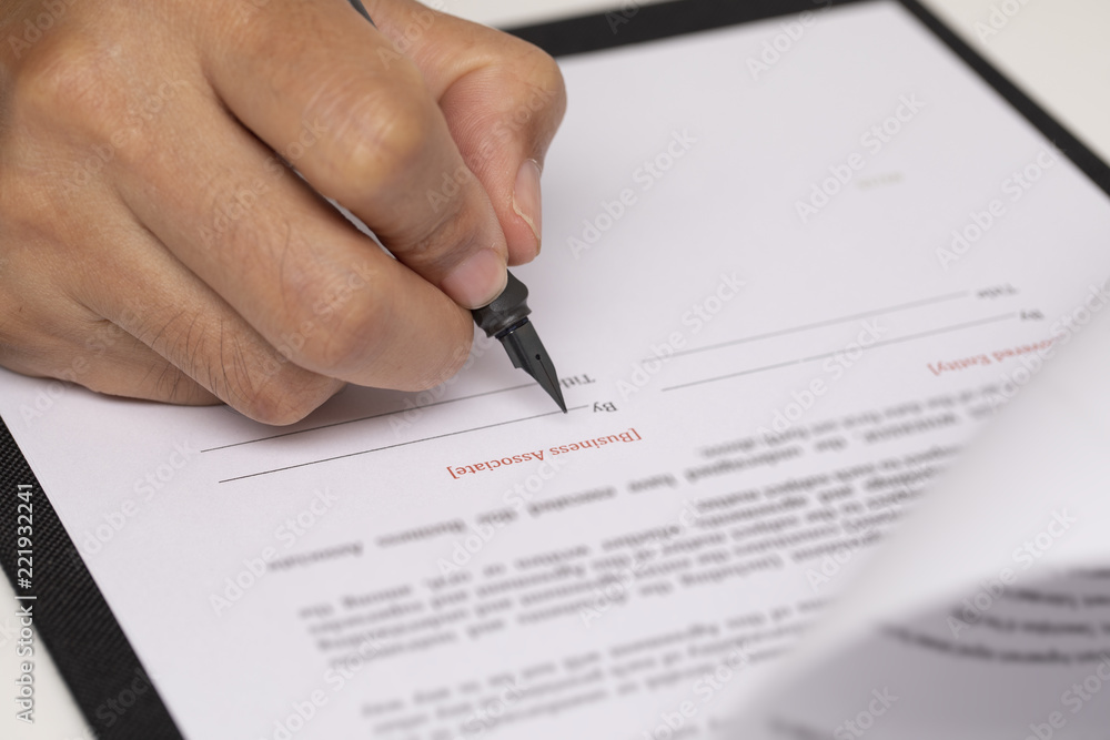 Hand signing official document with black pen on clipboard showcasing legal agreement authorization and formal paperwork process Hand signing official document with black pen on clipboard showcasing legal agreement authorization and formal paperwork process