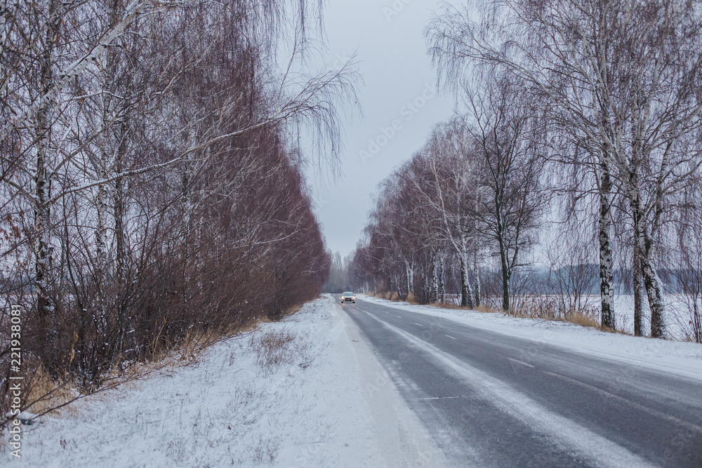 Snow-covered road with birches without foliage. Car on a slippery road. rolled track on first snow. Danger of drifts. Snow-covered road with birches without foliage. Car on a slippery road. rolled track on first snow. Danger of drifts.