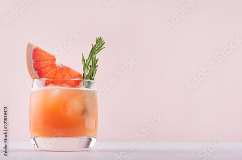Cold grapefruit cocktail decorated twig rosemary and slice citrus on pink background.