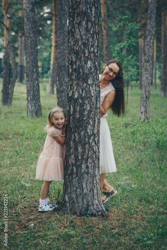 mom and daughter are hiding behind a tree. a woman and a little girl peeking out from behind a pine tree