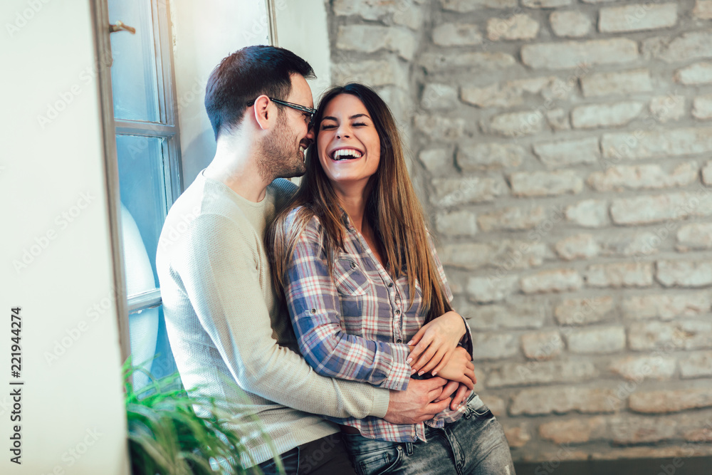 Naklejka premium Portrait of a young couple hugging next to the window, brick wall background.