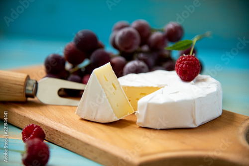 cheese camembert with raspberries and grapes on a blue