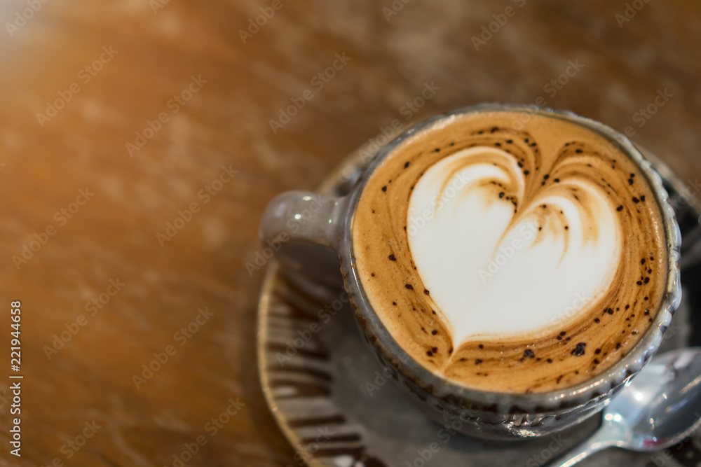 Fototapeta premium Hot coffee with heart-shaped froth on wooden table.