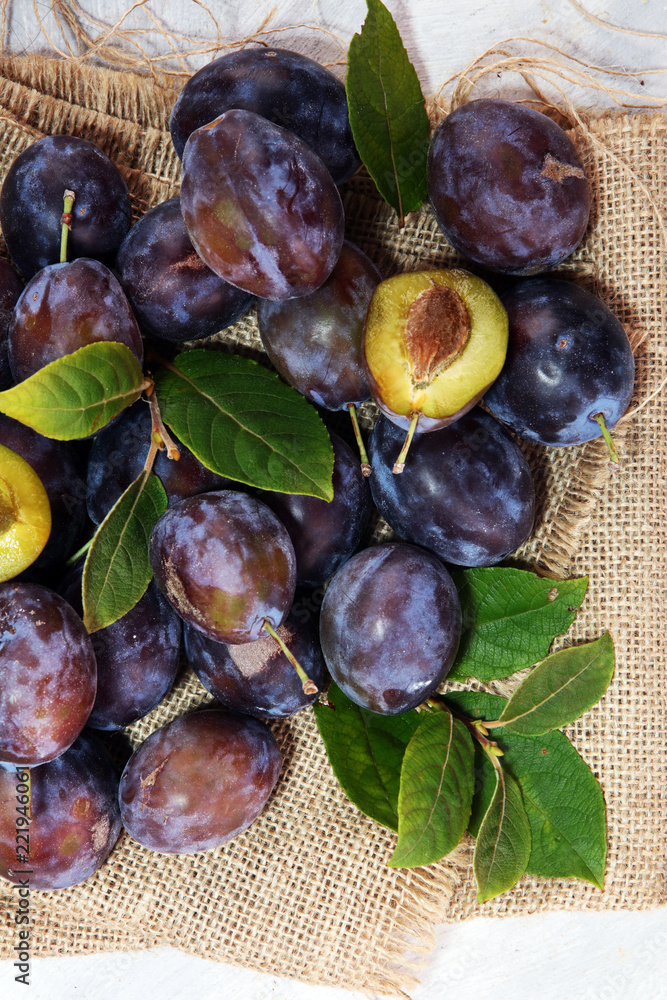 Fototapeta premium Plums on rustic background. Half of blue plum fruit. Many beautiful plums with leaves