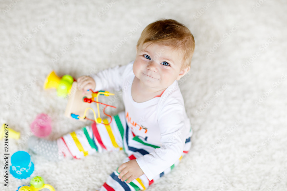 Adorable baby girl playing with educational toys in nursery. Happy healthy child having fun with colorful different toys at home. Baby development and first steps, learning to play and to grab. - obrazy, fototapety, plakaty 