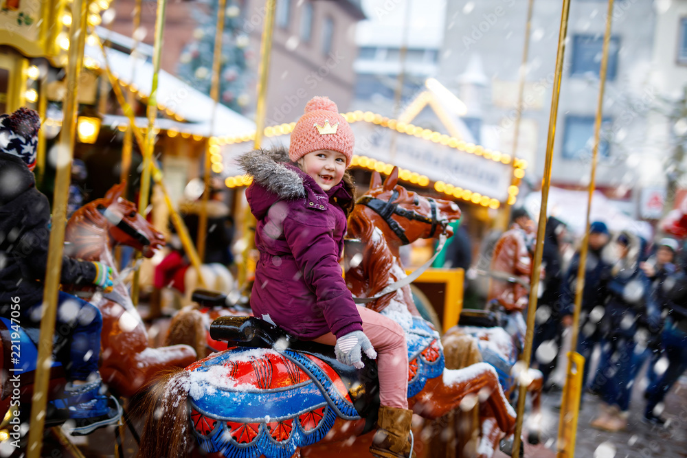 Naklejka premium Adorable little kid girl riding on a merry go round carousel horse at Christmas funfair or market, outdoors. Happy child having fun on traditional family xmas market in Dresden, Germany