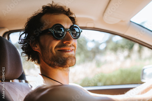 lächelnder weißer Mann mit Sonnenbrille fährt mit dem Auto in den Sommerurlaub 