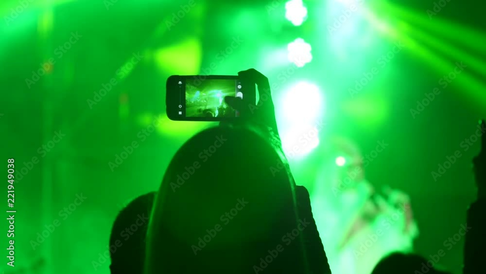 Spectator girl fan silhouette shooting a concert via smart phone in lumiere lights