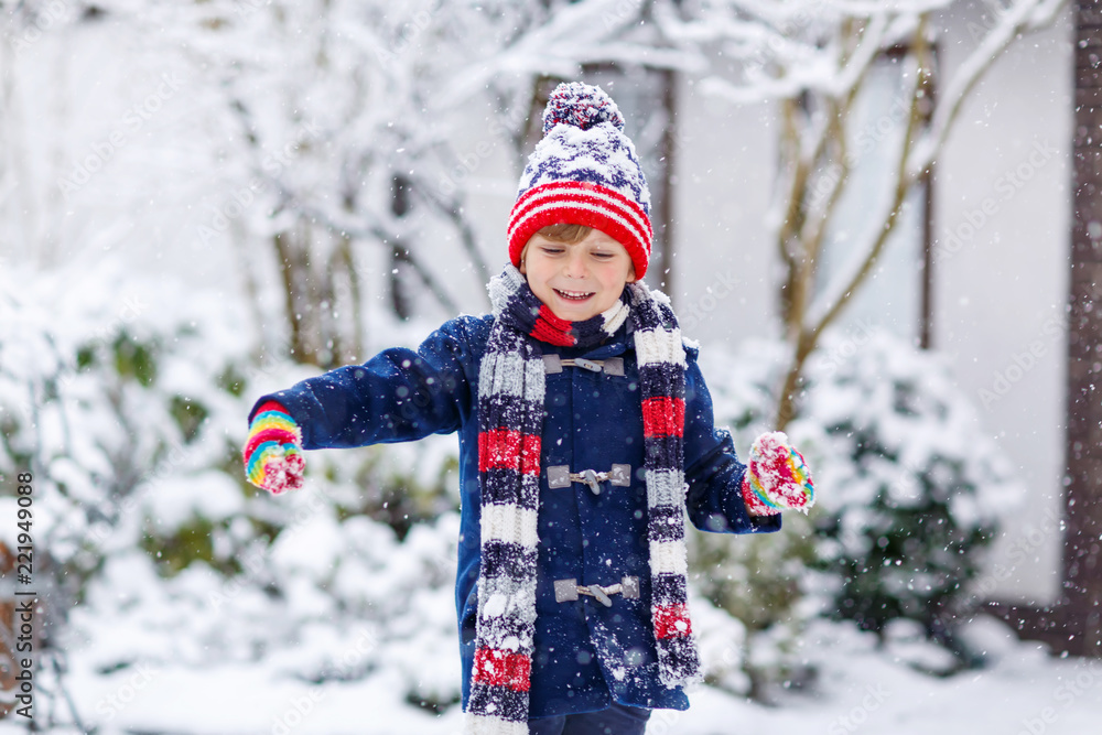 Cute little funny child in colorful winter fashion clothes having fun and  playing with snow, outdoors during snowfall. Active outdoors leisure with  children. Kid boy and toddler catching snowflakes. Stock Photo