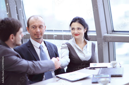 Smiling female and male business leaders handshaking over desk