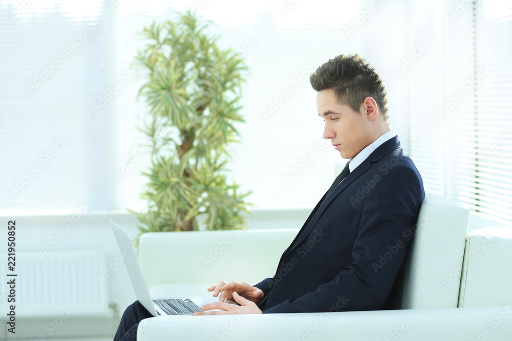 handsome businessman typing on laptop sitting in the lobby of th handsome businessman typing on laptop sitting in the lobby of th