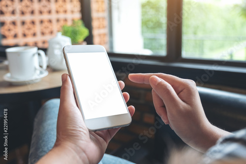 Mockup image of a woman's hands holding and pointing at white mobile phone with blank screen with coffee cup on table in modern cafe © Farknot Architect