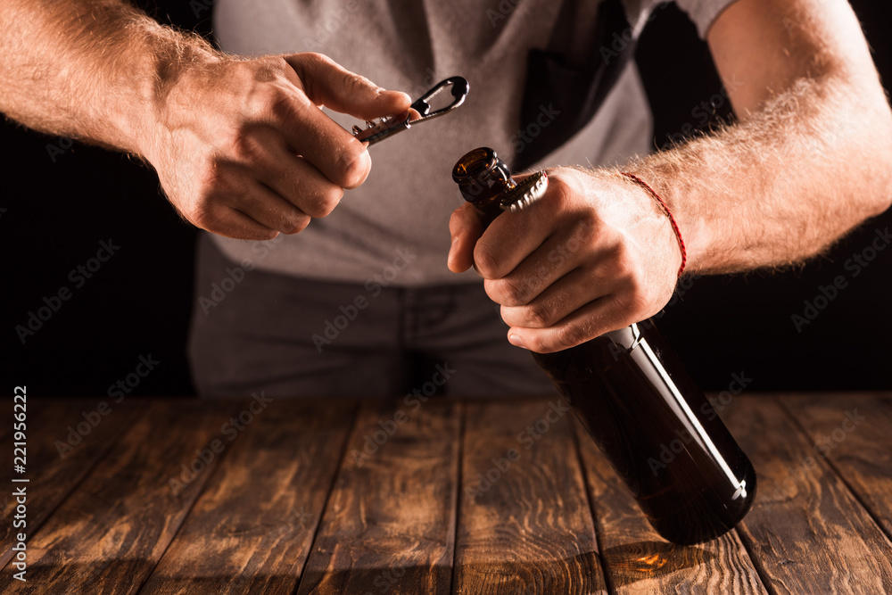 Fototapeta premium cropped image of man opening beer bottle by opener at wooden table