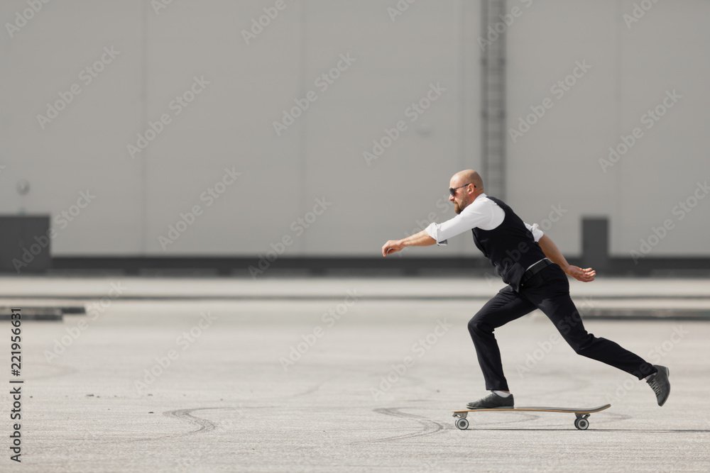 Young man on the fashion nice suit on the longboard skatebourd at the airport near modern building Young man on the fashion nice suit on the longboard skatebourd at the airport near modern building
