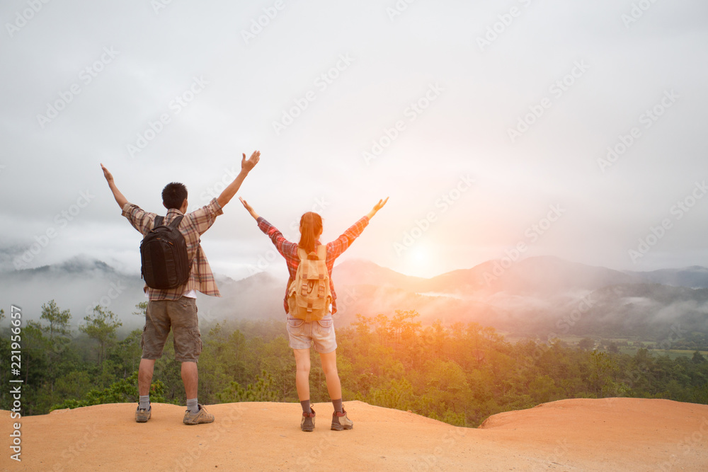 Hikers with backpacks relaxing on top of a mountain and enjoying the view of valley Hikers with backpacks relaxing on top of a mountain and enjoying the view of valley