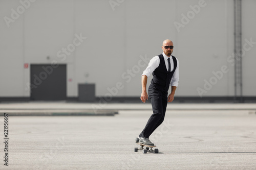 Young man on the fashion nice suit on the longboard skatebourd at the airport near modern building © Gennady Danilkin