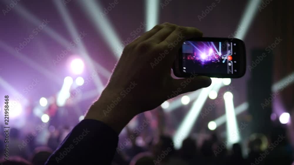 Fan spectator shooting video via smartphone camera at concert flashing lumiere Fan spectator shooting video via smartphone camera at concert flashing lumiere