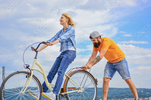 Woman rides bicycle sky background. How to learn to ride bike as an adult. Girl cycling while boyfriend support her. Teach adult to ride bike. Man helps keep balance and ride bike. Find balance