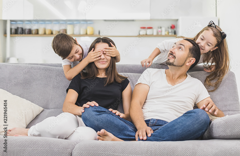 Happy parents and kids having fun sitting together on sofa, cheerful couple laughing playing game with little active children son and daughter in living room at home, family funny activity Happy parents and kids having fun sitting together on sofa, cheerful couple laughing playing game with little active children son and daughter in living room at home, family funny activity