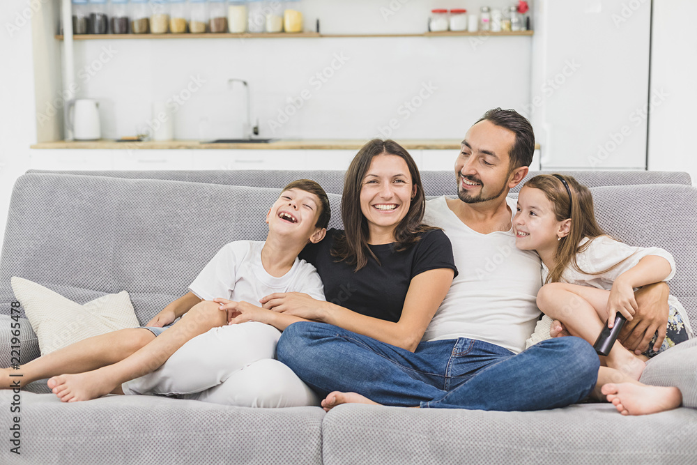 Family sitting on sofa smiling at camera on modern apartment background Family sitting on sofa smiling at camera on modern apartment background
