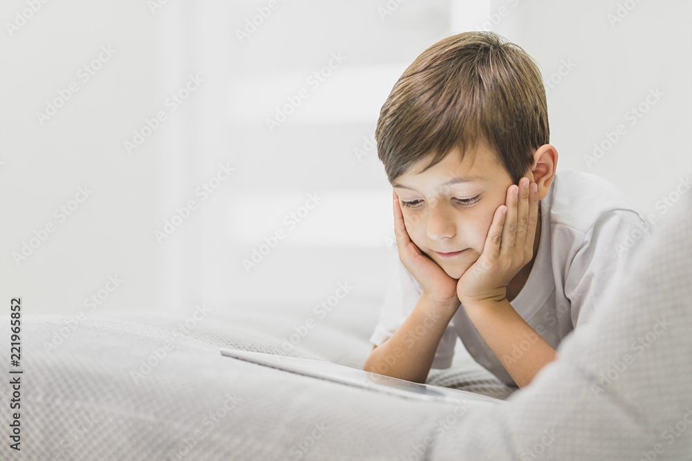 Active little boy sitting on sofa watching tablet , Happy kid boy relaxing on sofa on a bright sunny say, Child with technology concept Active little boy sitting on sofa watching tablet , Happy kid boy relaxing on sofa on a bright sunny say, Child with technology concept