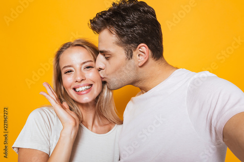 Loving couple standing isolated over yellow wall background take a selfie by camera.