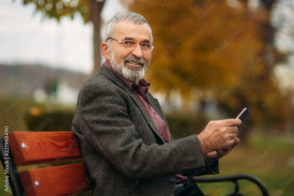 Grandpa uses a tablet sitting in the park on the bench Grandpa uses a tablet sitting in the park on the bench