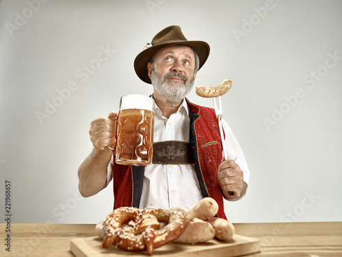 Germany, Bavaria, Upper Bavaria. The senior happy smiling man with beer dressed in traditional Austrian or Bavarian costume holding mug of beer at pub or studio. The celebration, oktoberfest, festival