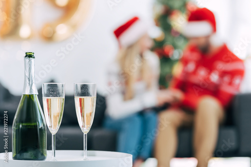 selective focus of champagne bottle and glasses for celebrating christmas, couple sitting behind