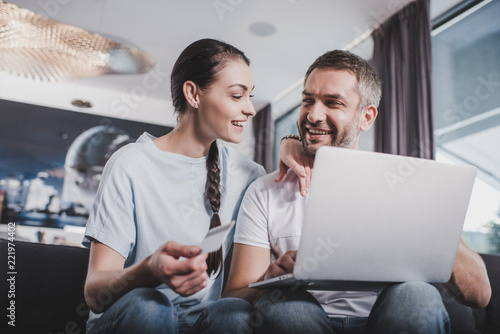 happy couple with laptop doing online shopping by credit card at home