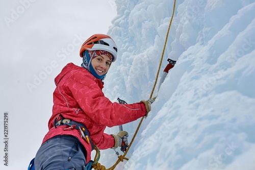 Alpinist woman with  ice tools axe in orange helmet climbing a l