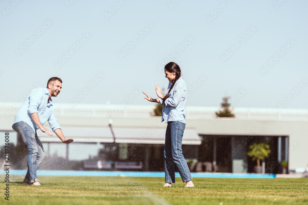 Obraz premium couple having fun with automatic watering on green lawn near country house