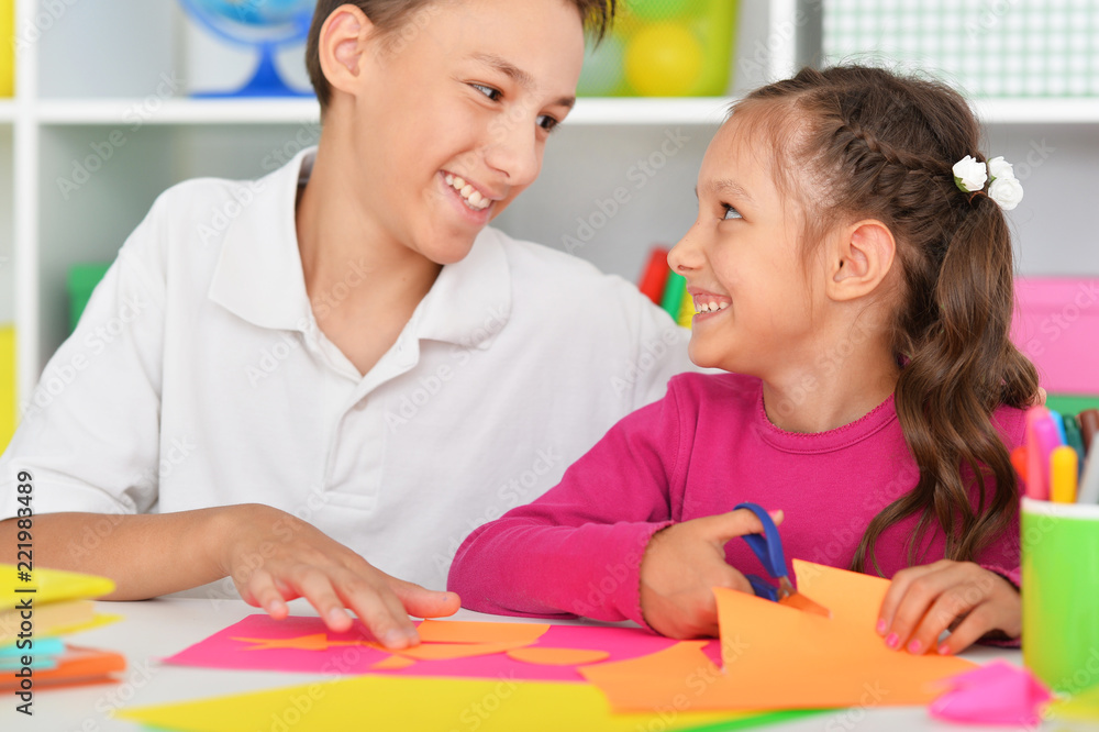 Cute brother and sister gluing and cutting colorful paper