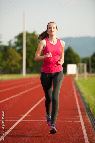 Beautiful young woman runner run on a track in early summer afternoon