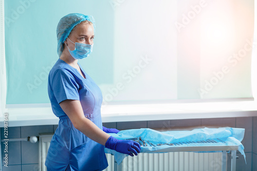 Foto Young blond woman assistant standing near table with equipment prepating for gynecology operation