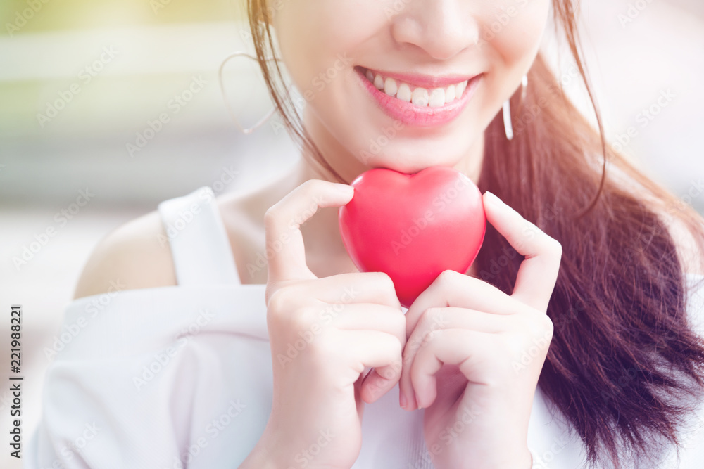 Asian teenage girls wearing white clothes smiling with a bright, relaxed, holding a red heart model represents an oral care for brushing the right way. Make a beautiful tooth. concept Dental Asian teenage girls wearing white clothes smiling with a bright, relaxed, holding a red heart model represents an oral care for brushing the right way. Make a beautiful tooth. concept Dental