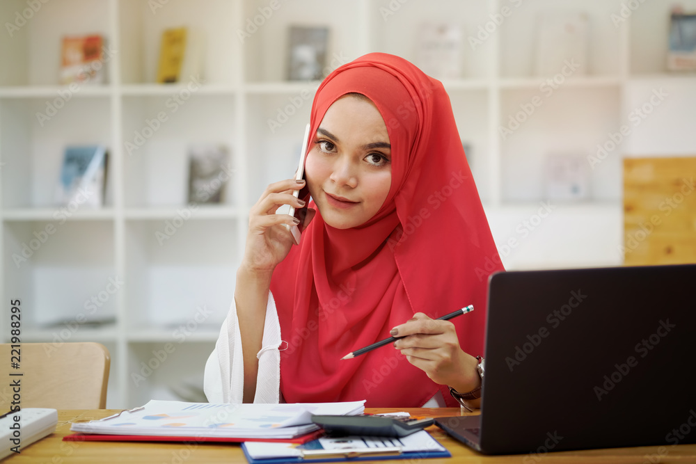 Young muslim businesswoman calling her mobile smartphone at workspace desk. Young muslim businesswoman calling her mobile smartphone at workspace desk.