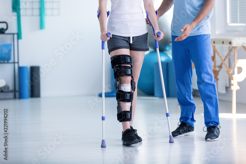 Fototapeta Sport physiotherapist and patient with leg injury during training with crutches