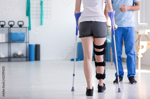 Slika na platnu Patient with stiffener on the leg walking with crutches during rehabilitation