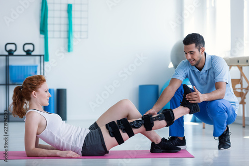 Photos Woman with leg injury on mat and smiling doctor during treatment in the hospital