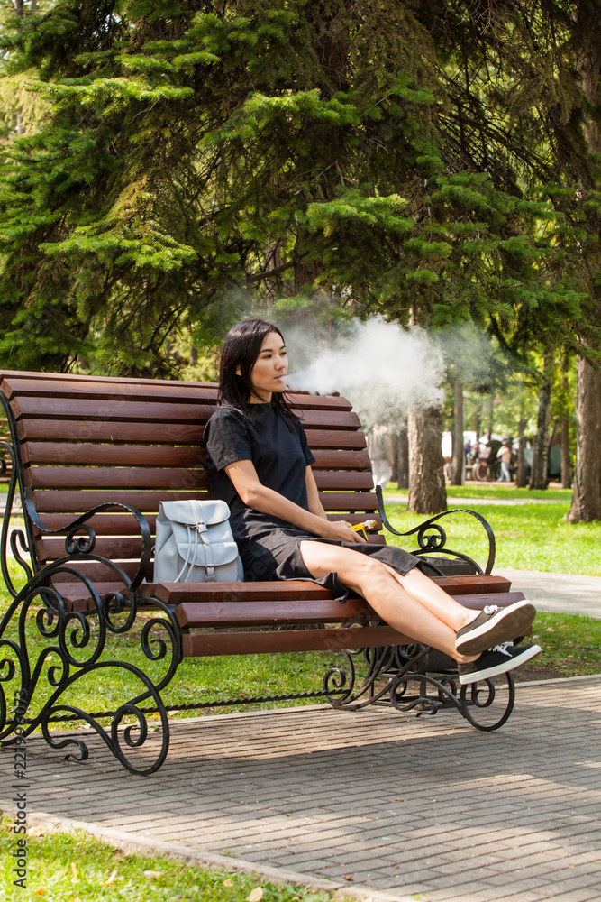 Asian on a park bench smokes a wipe. Harm from smoking Asian on a park bench smokes a wipe. Harm from smoking
