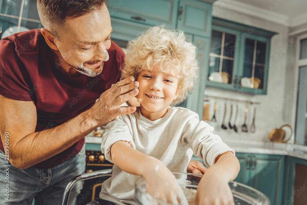 Obraz premium Caring father. Caring dark-haired father looking at his curly blonde-haired son while baking pastry together