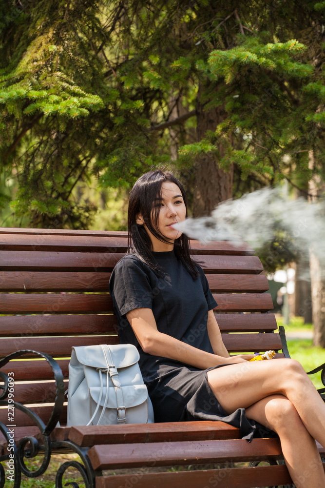 Asian on a park bench smokes a wipe. Harm from smoking Asian on a park bench smokes a wipe. Harm from smoking