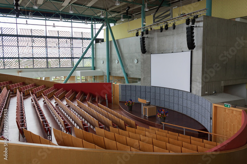 A large lecture hall at the university or at school. Tribune, screen for presentations and a cascade of chairs for students.