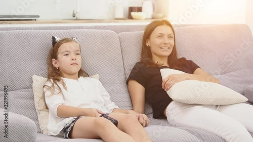 Mother and daughter are having a lot of fun and talking while watching TV in the living room sitting on the couch. mother and daughter holding hands. Close up