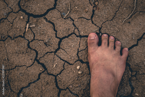 Foot on Dried cracked earth soil ground texture background.