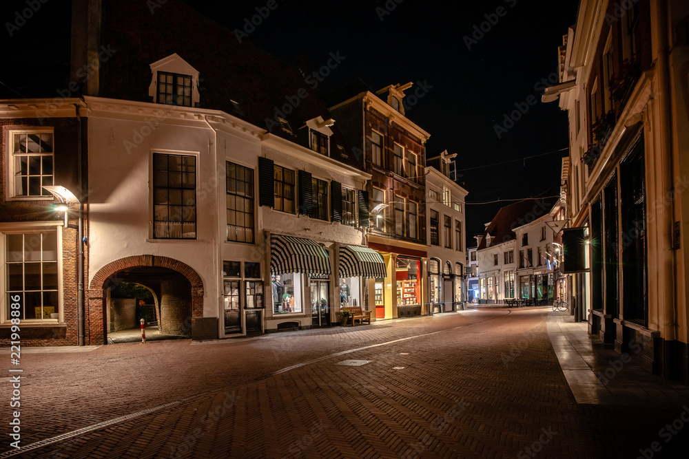 Cozy winding shopping street with illuminated shops in a characteristic medieval town. Monumental medieval houses in Historic old fortified town in the Netherlands 