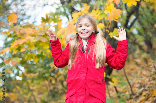 Cheerful schoolgirl. Child blonde long hair walking in warm jacket outdoor. Girl happy in red coat enjoy fall nature park. Child wear fashionable coat with hood. Fall clothes and fashion concept